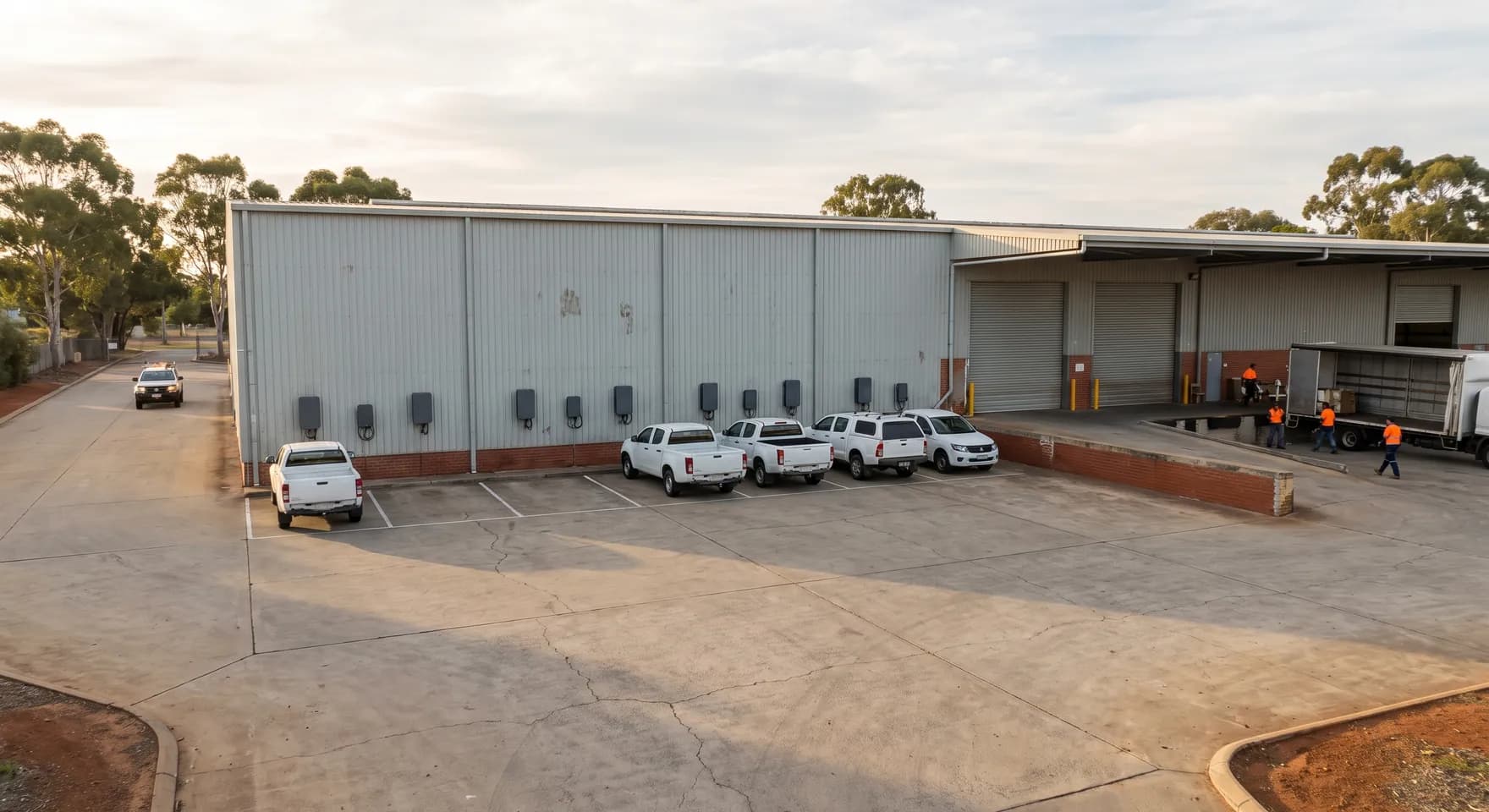 A row of chargers along the wall of a Balcatta distribution warehouse with delivery utes parked nose in on the hardstand