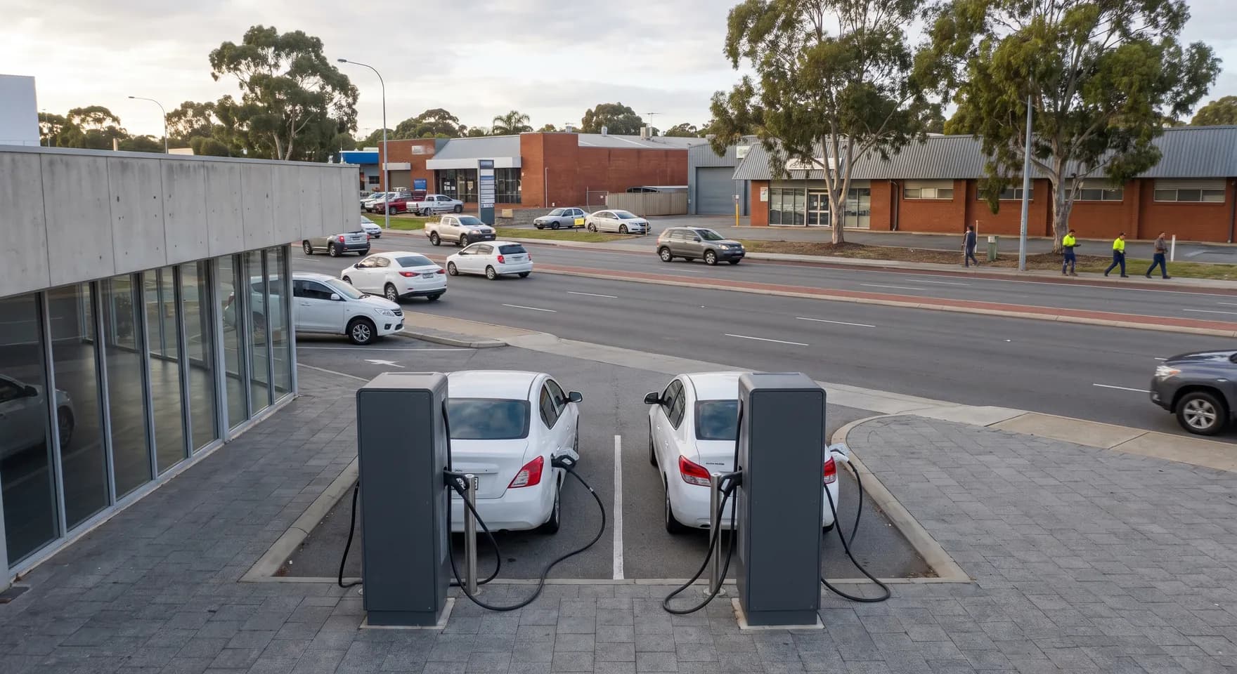 Two pedestal chargers in customer bays at the front of a Myaree showroom, with the highway and low retail buildings behind