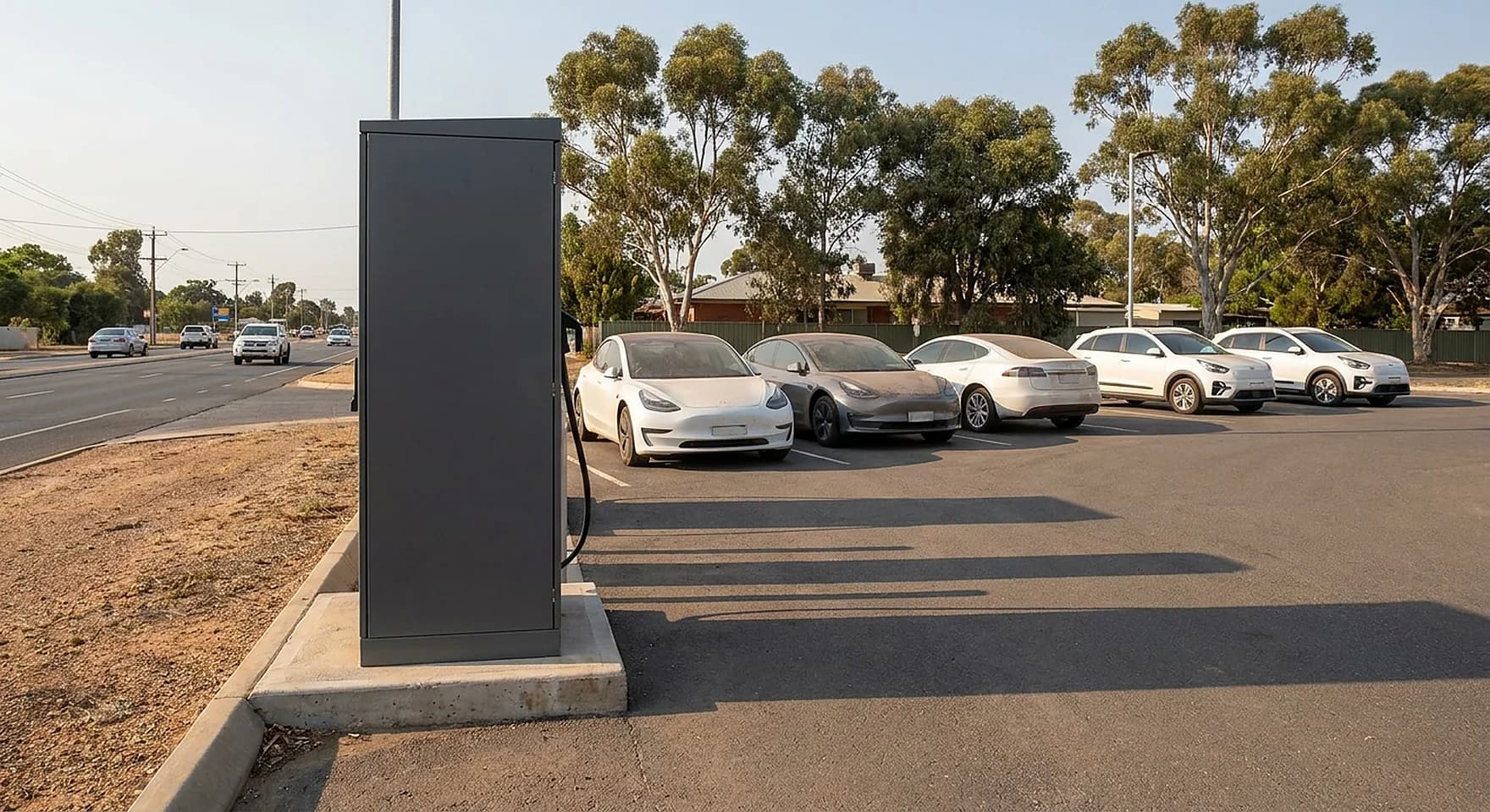 A DC fast charging cabinet on a concrete plinth at the edge of a car dealership forecourt in Osborne Park