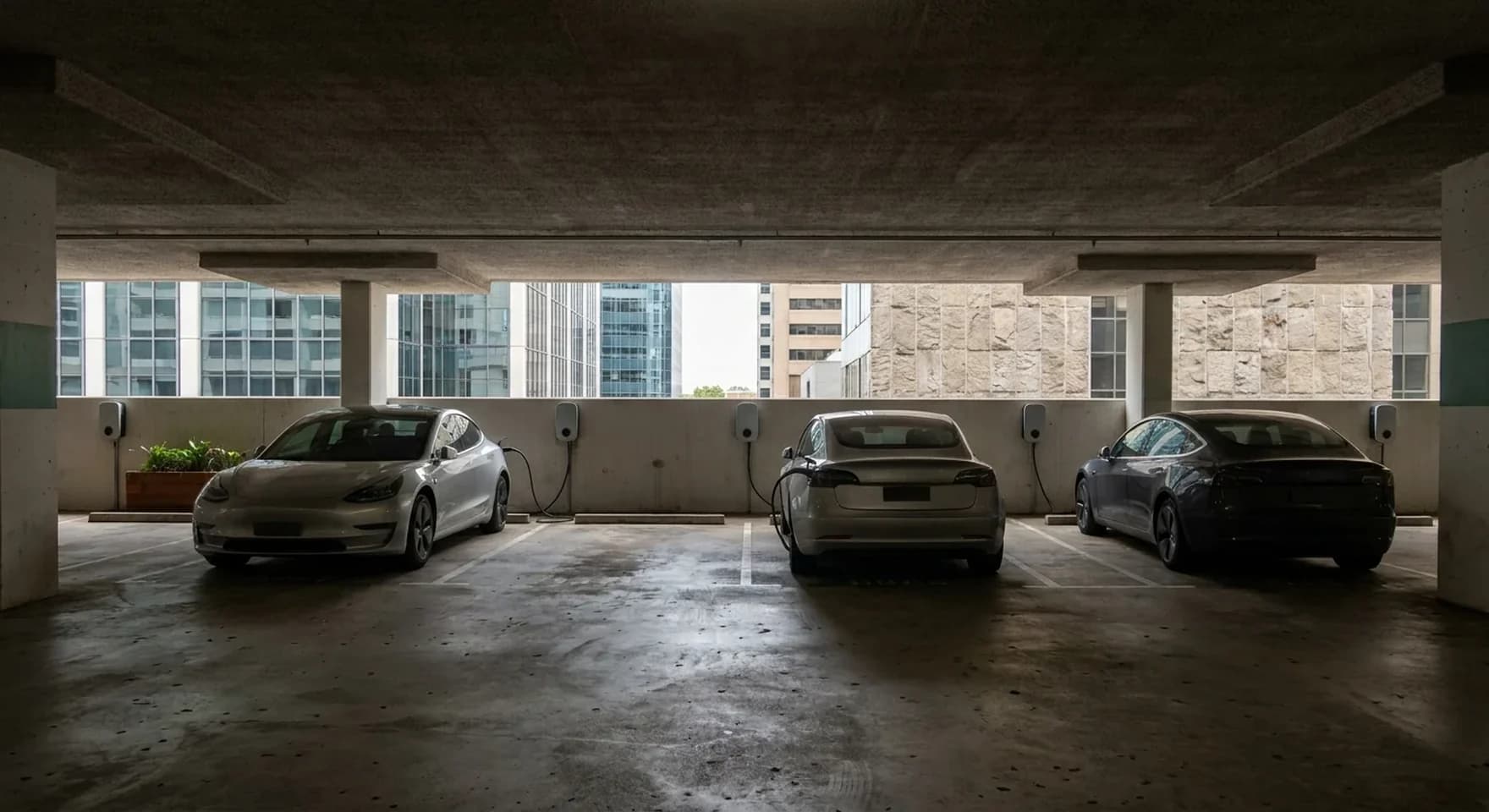 Wall mounted EV chargers above marked bays in a Perth CBD office tower carpark, city towers visible through the open end of the deck